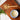 Overhead view of a wooden spoon labeled “Full Leaf Tea Co.” filled with dried astragalus root pieces on a wooden board next to a cup of tea with a blue rim and fresh green herbs.