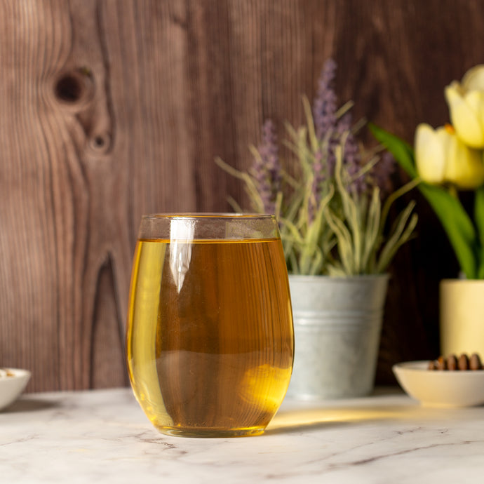 Glass of Organic Bladder Health Tea on a marble surface with flowers and herbs in the background.