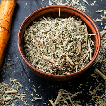 Bowl of dried herbal tea leaves on a dark surface with scattered pieces around.