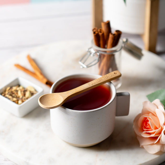 Cup of brewed Organic Blood Pressure Tea with a wooden spoon, cinnamon sticks, and loose tea ingredients on a marble surface.