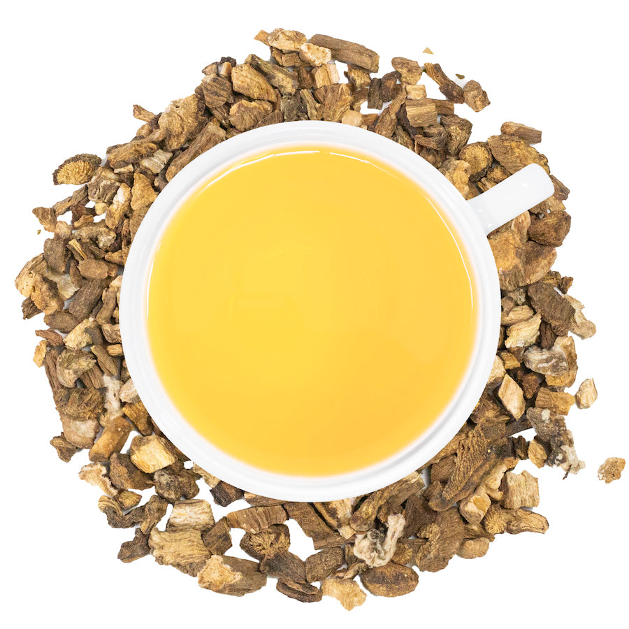 A white mug filled with burdock tea surrounded by burdock.