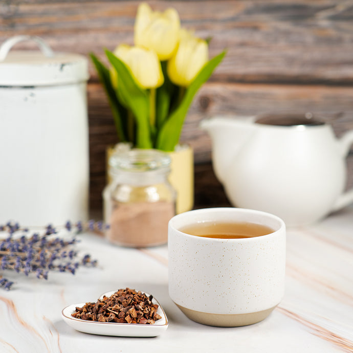 White ceramic mug with tea, teapot, and flowers on a wooden table