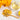 Wooden spoon filled with dried yellow calendula petals beside a glass cup of golden calendula tea, with fresh yellow flowers and a lemon on a white marble surface.