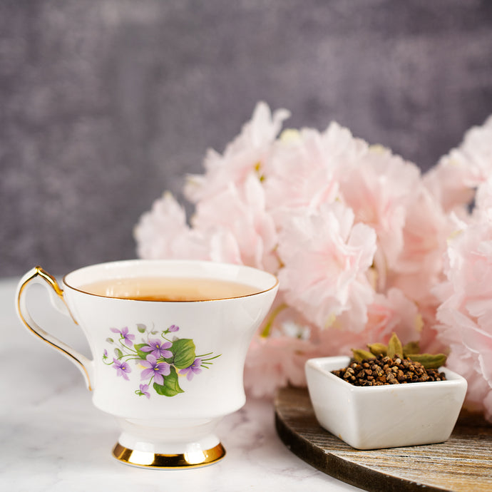 Teacup with floral design on a marble surface with pink flowers in the background