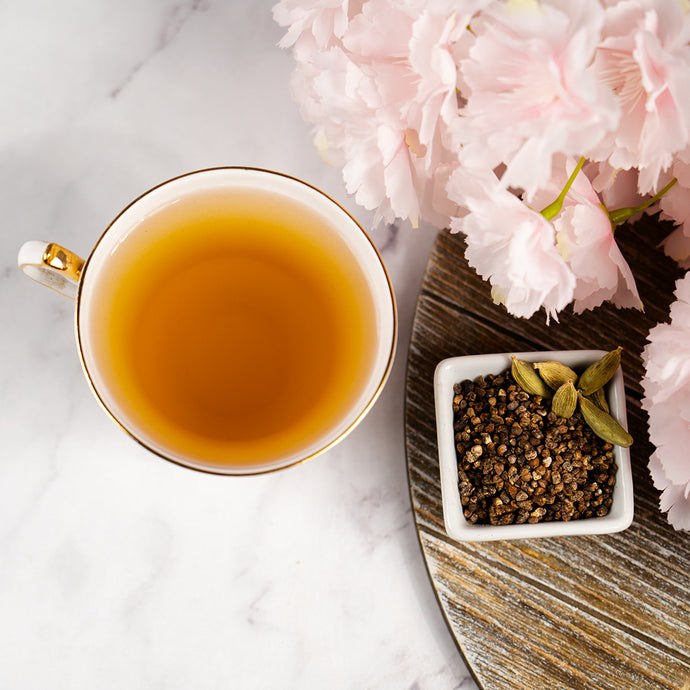 Tea cup with cardamon seeds on a marble surface with pink flowers