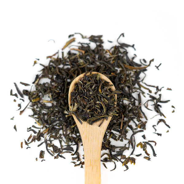 A wooden spoon with ceylon green herbs spread on it and around it. 