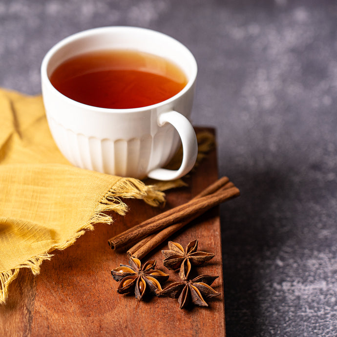 White mug of tea on a wooden board with cinnamon sticks and star anise, against a dark background.