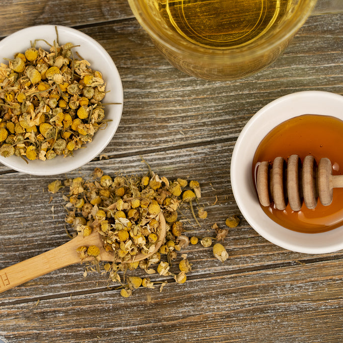 Organic Bladder Health Tea with dried chamomile flowers, honey, and a cup of brewed tea on a rustic wooden surface.