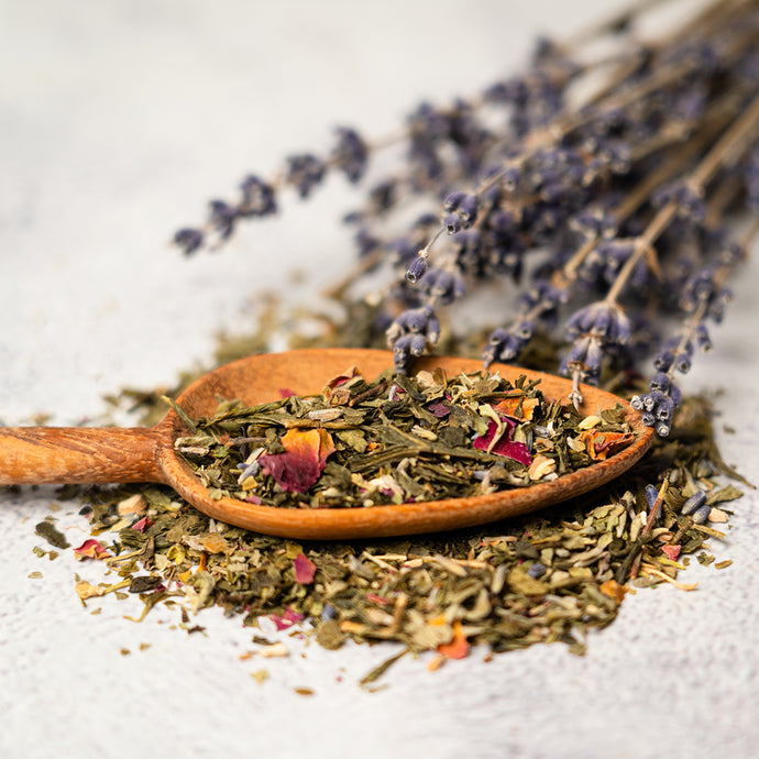 Wooden spoon with cheerful tea herbs on a white surface with lavender in the background