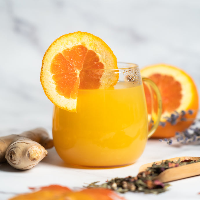 Glass of cheerful autumn elixir with a slice of orange on a white surface with ginger and oranges.