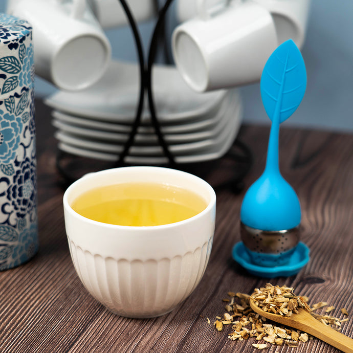 Tea cup with blue tea infuser and chicory root on a wooden surface