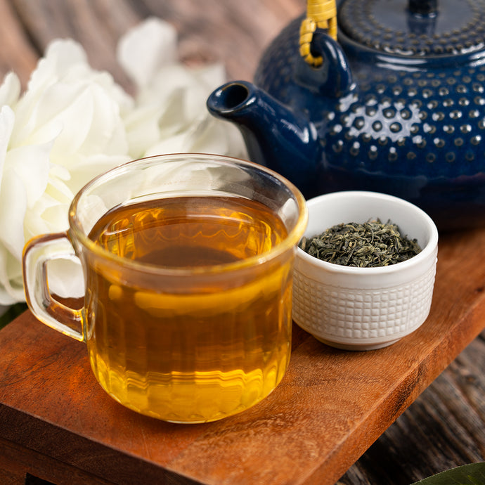 Tea cup with tea, teapot, and bowl of china green tea leaves on a wooden surface