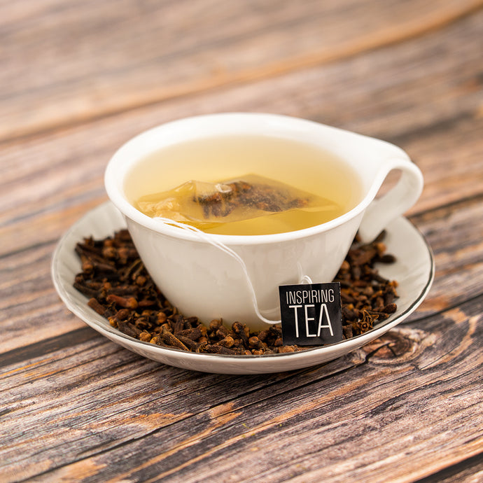 White teacup with tea leaves and a 'Inspiring Tea' tag on a wooden surface