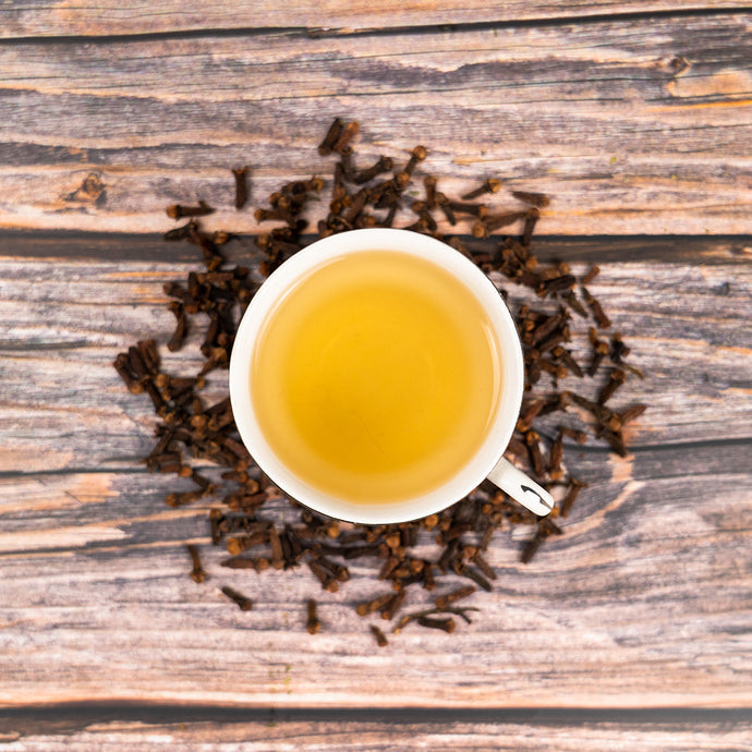 White cup of tea surrounded by cloves on a wooden surface