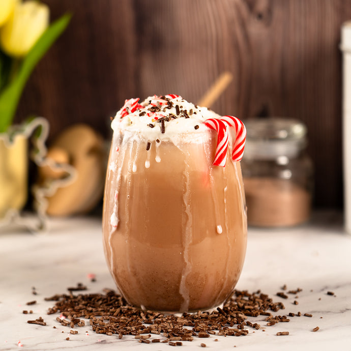 Chocolate drink with whipped cream and a candy cane in a glass on a marble surface.