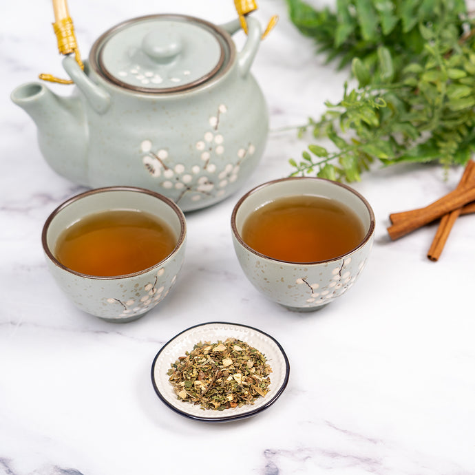 Tea set with two cups, a teapot, and a small plate of congestion relief tea on a marble surface.