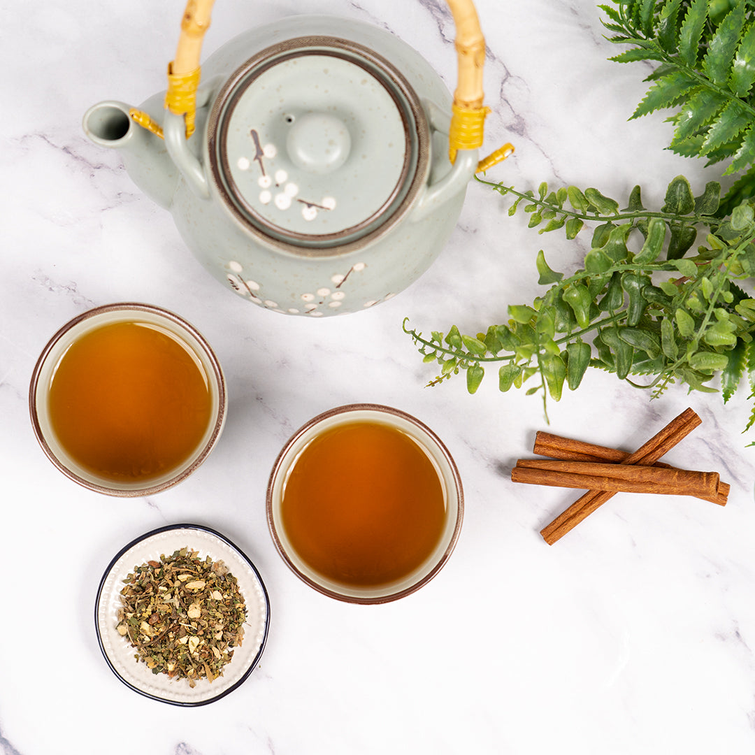 Congestion Relief Tea served in ceramic cups with a matching teapot, loose herbal blend, cinnamon sticks, and green foliage on a marble surface.