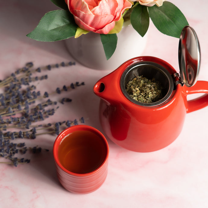 Red teapot with a cup and dried lavender on a pink surface