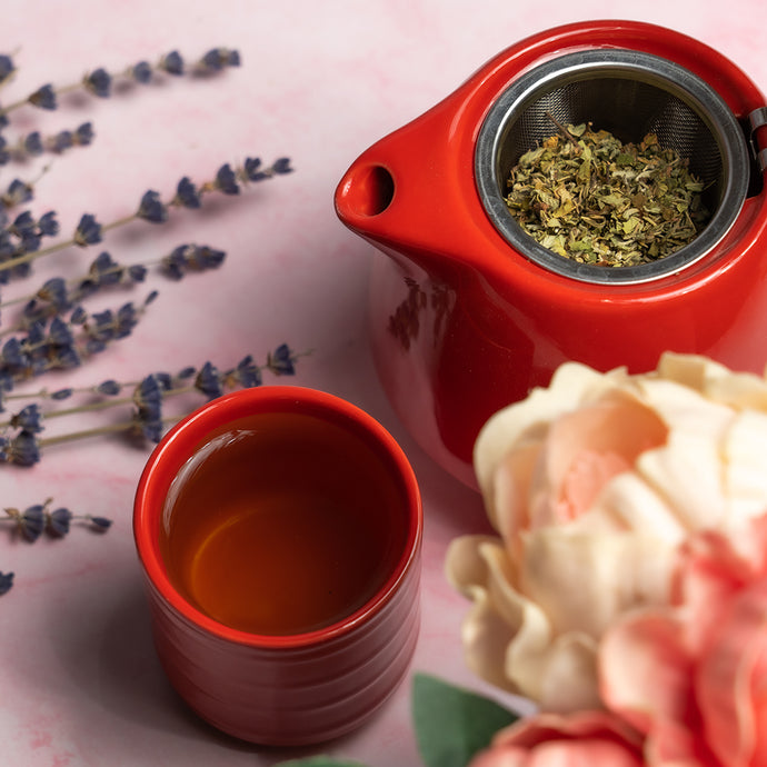 Red teapot with a cup of tea and lavender flowers on a pink surface