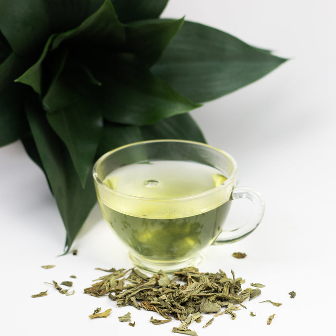 Clear glass cup of decaf sencha green tea with tea leaves on a white background