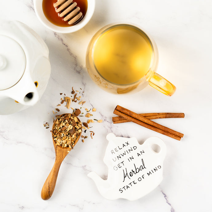 Tea-making setup with a mug, teapot, cinnamon sticks, and a decorative sign on a marble surface.