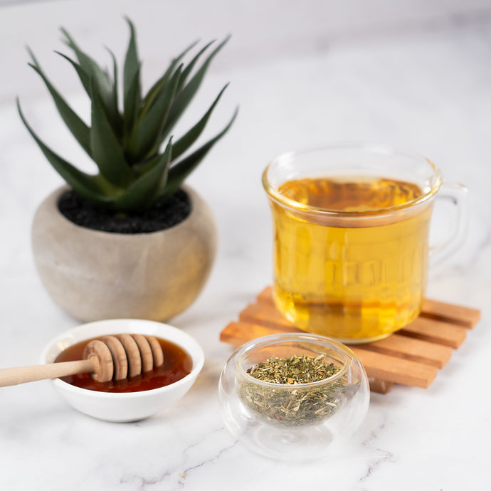 Glass of tea with honey, herbs, and a small plant on a marble surface