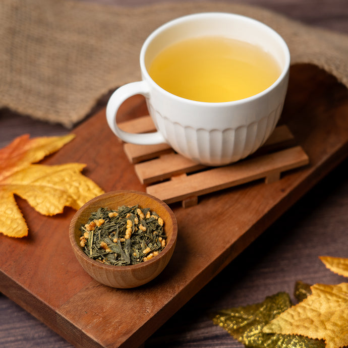 White mug of tea on a wooden tray with a bowl of tea leaves and autumn leaves.