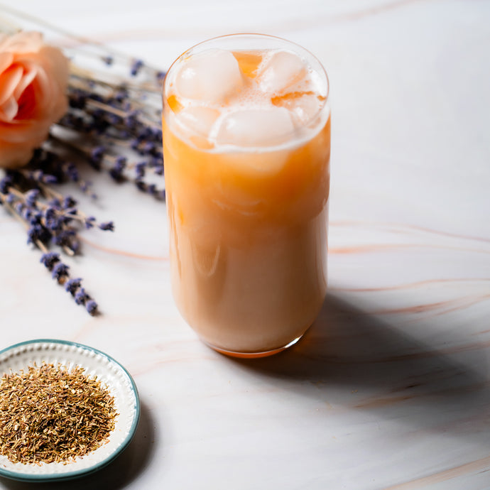 Glass of iced green rooibos spring bliss with flowers and a bowl of spices on a marble surface