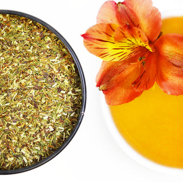 Green rooibos herbs next to a green rooibos tea blend on top of a white surface. 