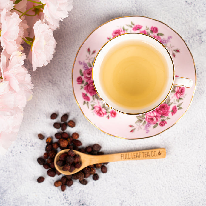 Tea cup with floral design on a saucer, surrounded by tea leaves and a wooden spoon with 'Full Leaf Tea Co.' branding.