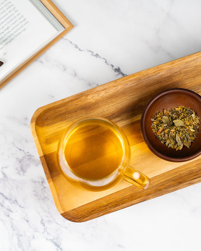 Glass of healthy vision tea on a wooden tray with a bowl of tea leaves on a marble surface
