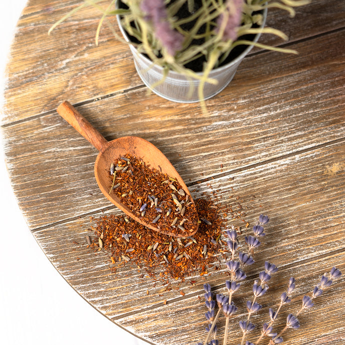 Wooden scoop with dried hearbal earl on a wooden surface with lavender flowers.