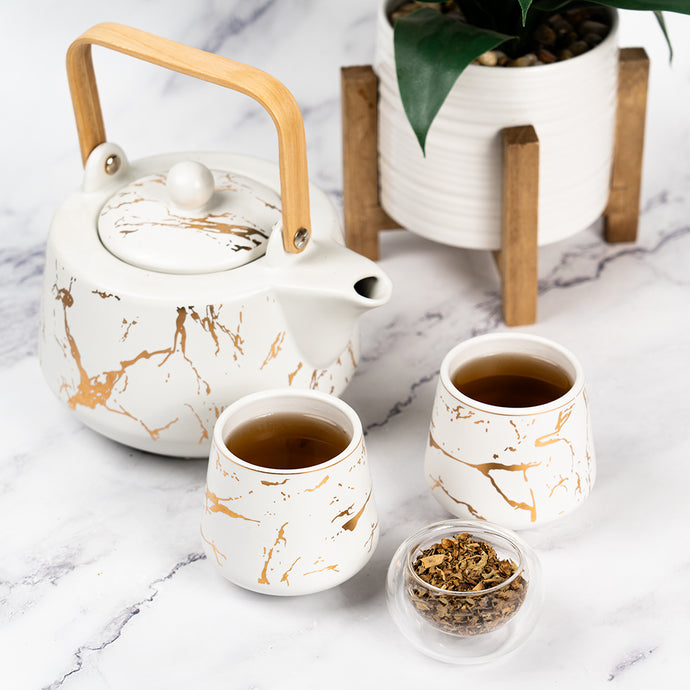 A ceramic teapot with a wooden handle and two matching cups filled with Organic Blood Pressure Tea, placed on a marble surface with a small glass dish of loose leaf tea beside them.