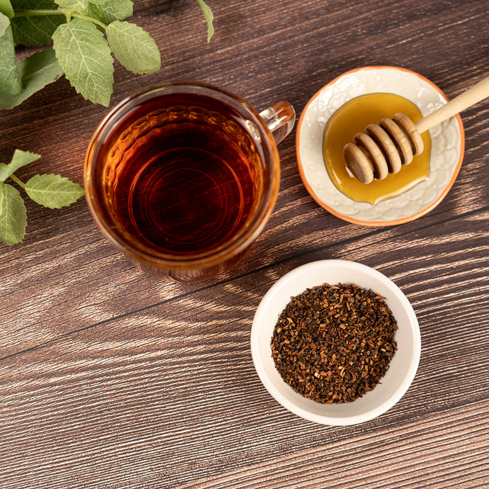 Cup of Blood Orange Black Tea with loose tea leaves, honey, and fresh mint on a wooden surface.