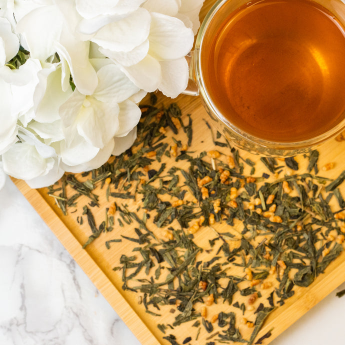 Tea leaves on a wooden board with a glass of tea and white flowers on a marble surface