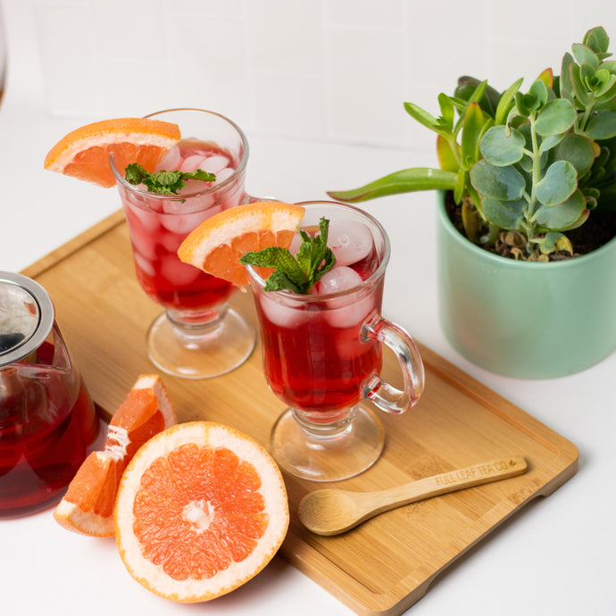 Two glasses of tea with ice and orange slices on a wooden board, accompanied by a potted plant.