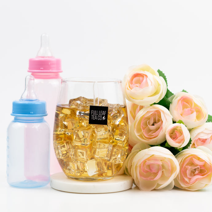 Glass of iced tea with ice cubes, baby bottles, and flowers on a white background