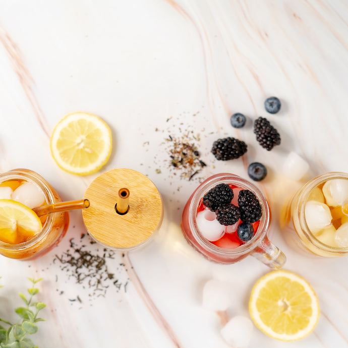 Three glasses of iced tea with lemon slices, berries, and ice cubes on a light wooden surface.