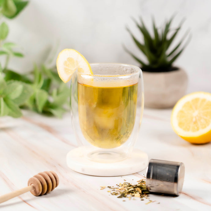 Glass of jade bliss tea with a slice of lemon on a wooden table with plants in the background