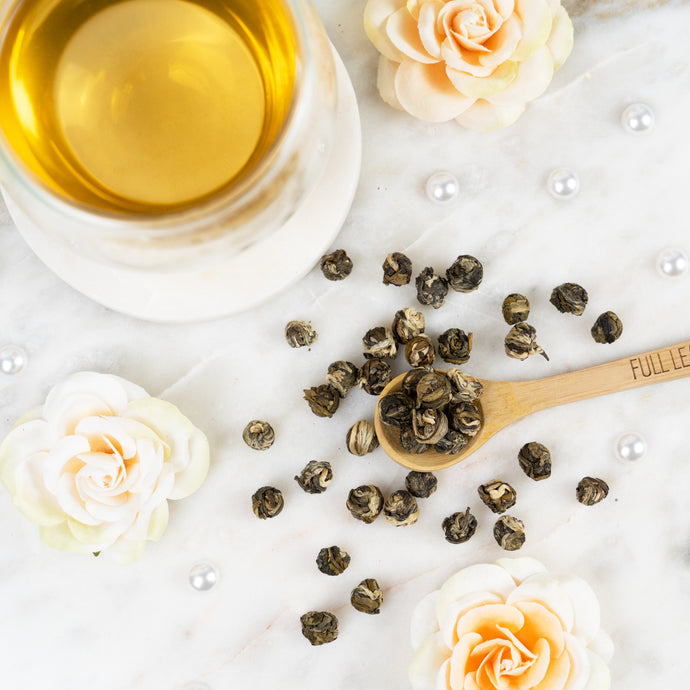 Jasmine pearls on a wooden spoon with a cup of tea and flowers on a white surface