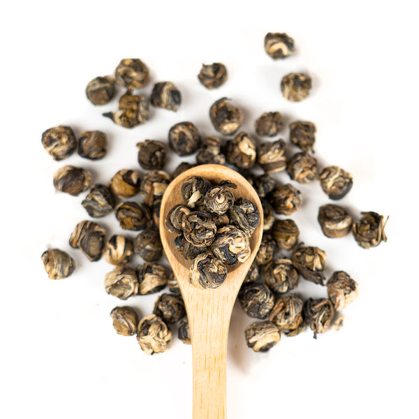 Wooden spoon of Organic Jasmine Pearls on a white background.