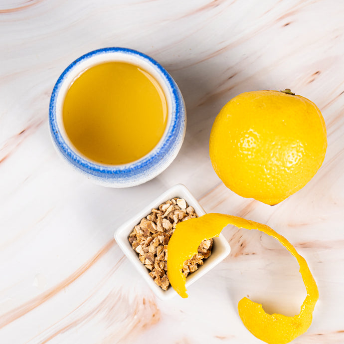 Small bowl of lemon peel tea, lemon, and lemon peel on a light wooden surface