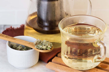 A cup of mullein tea with mullein herbs in a cup besides it. 