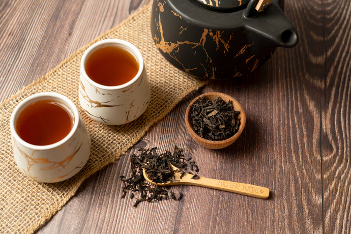 Tea cups, teapot, and oolong tea leaves on a wooden surface