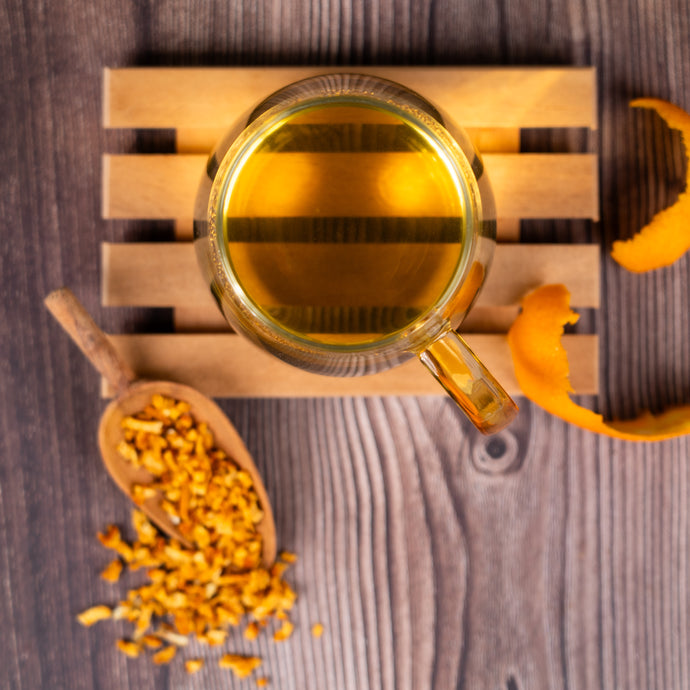 Cup of herbal tea on a wooden mat with dried orange peel and zest on a wooden surface.