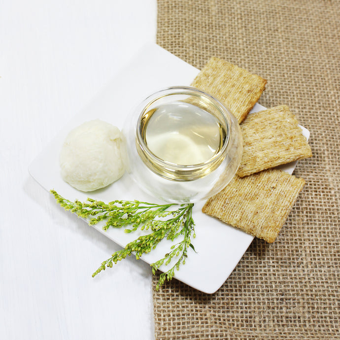 Glass of white wine with a cheeseboard featuring a cheese ball and crackers on a textured surface.