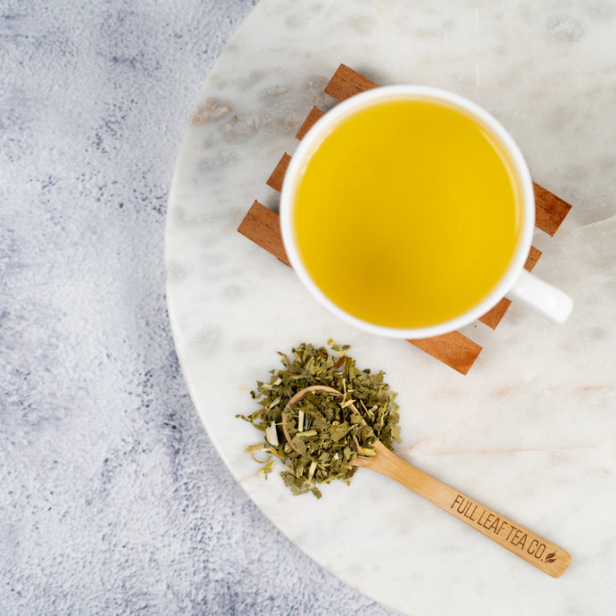 White mug with Passion Flower tea on a marble coaster with dried herbs and a wooden spoon.