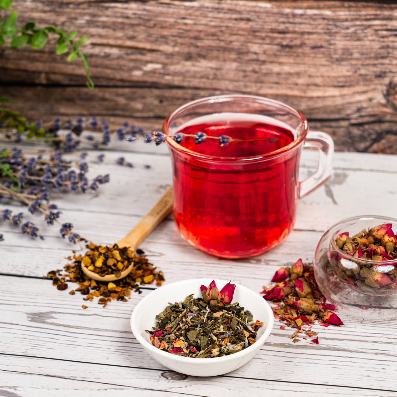 Pink tea in a glass mug with dried herbs and flowers on a wooden surface