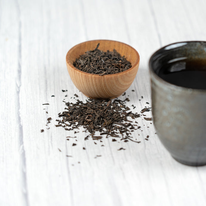 Wooden bowl with Pu-Erh tea leaves and a black ceramic cup on a white surface