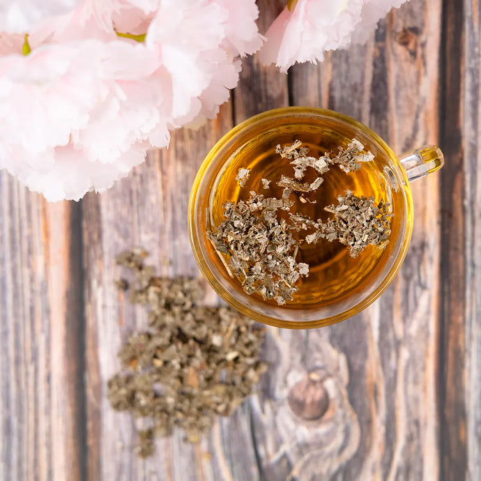 Cup of tea with dried raspberry leaf on a wooden surface with cherry blossoms.